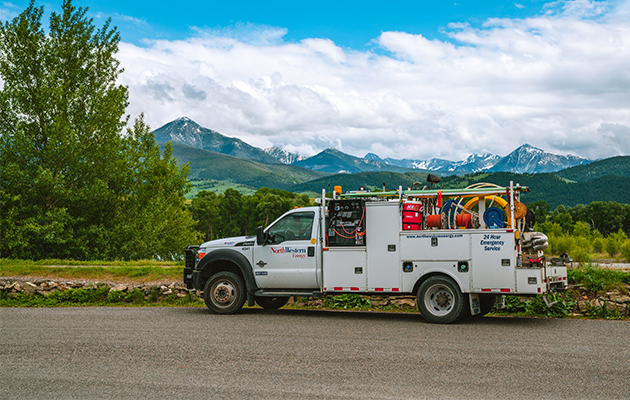 NorthWestern Energy service truck parked along a road with mountains and trees in the background.
